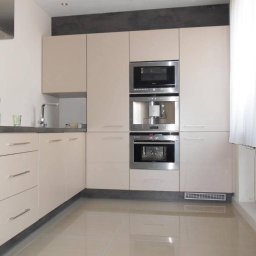 F.U.H.Armex Artur Piotrowski - Jasna kuchnia z zabudową meblową, w której zintegrowano piekarnik, ekspres do kawy i mikrofalówkę; widoczna butelka wody mineralnej na blacie.