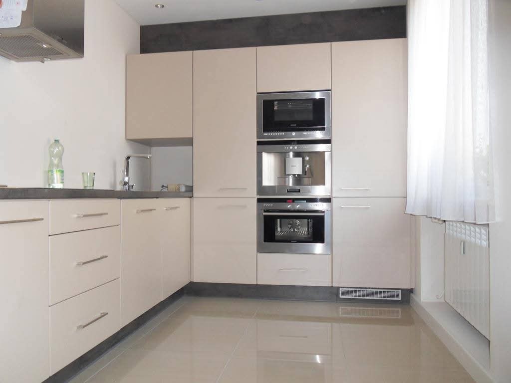 Jasna kuchnia z zabudową meblową, w której zintegrowano piekarnik, ekspres do kawy i mikrofalówkę; widoczna butelka wody mineralnej na blacie.