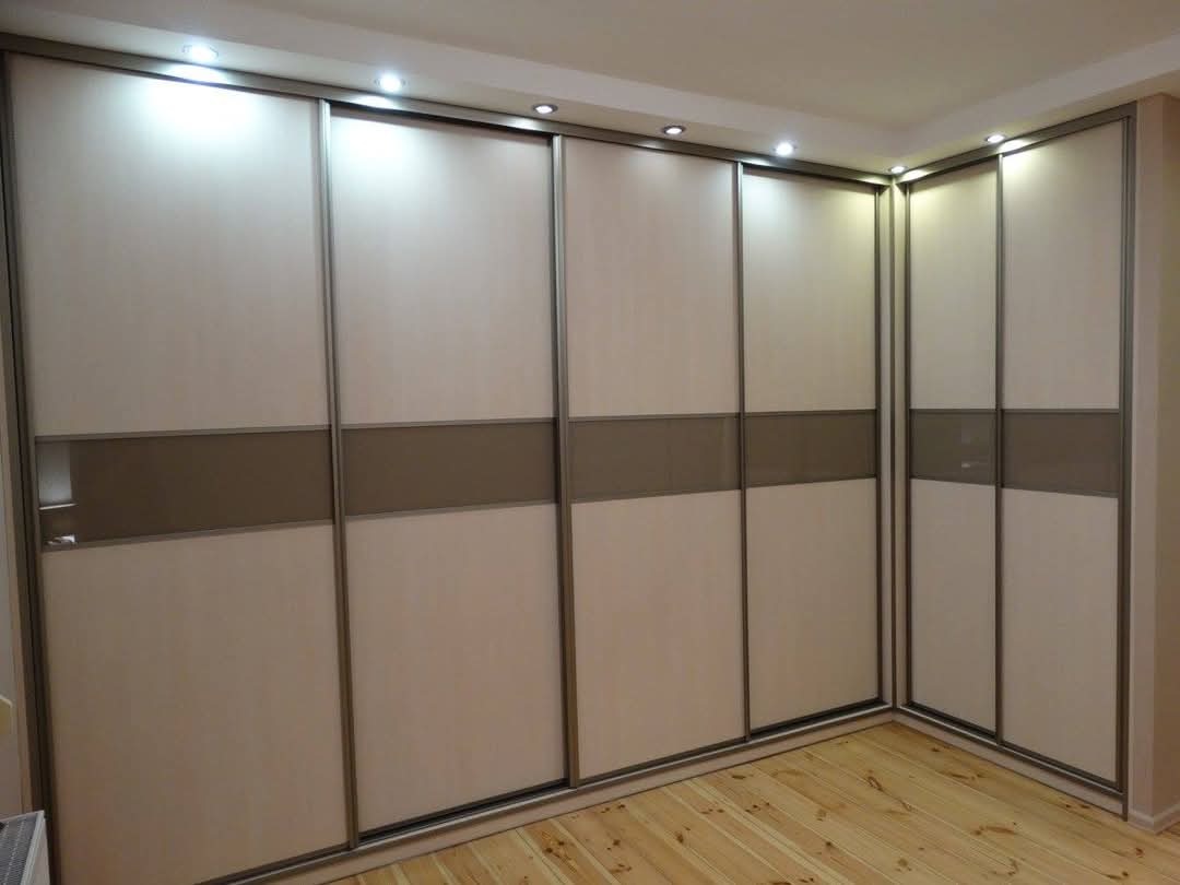 Duża szafa wnękowa z przesuwnymi drzwiami, jasnymi panelami i poziomym pasem w kolorze taupe, oświetlenie punktowe na suficie, drewniana podłoga.