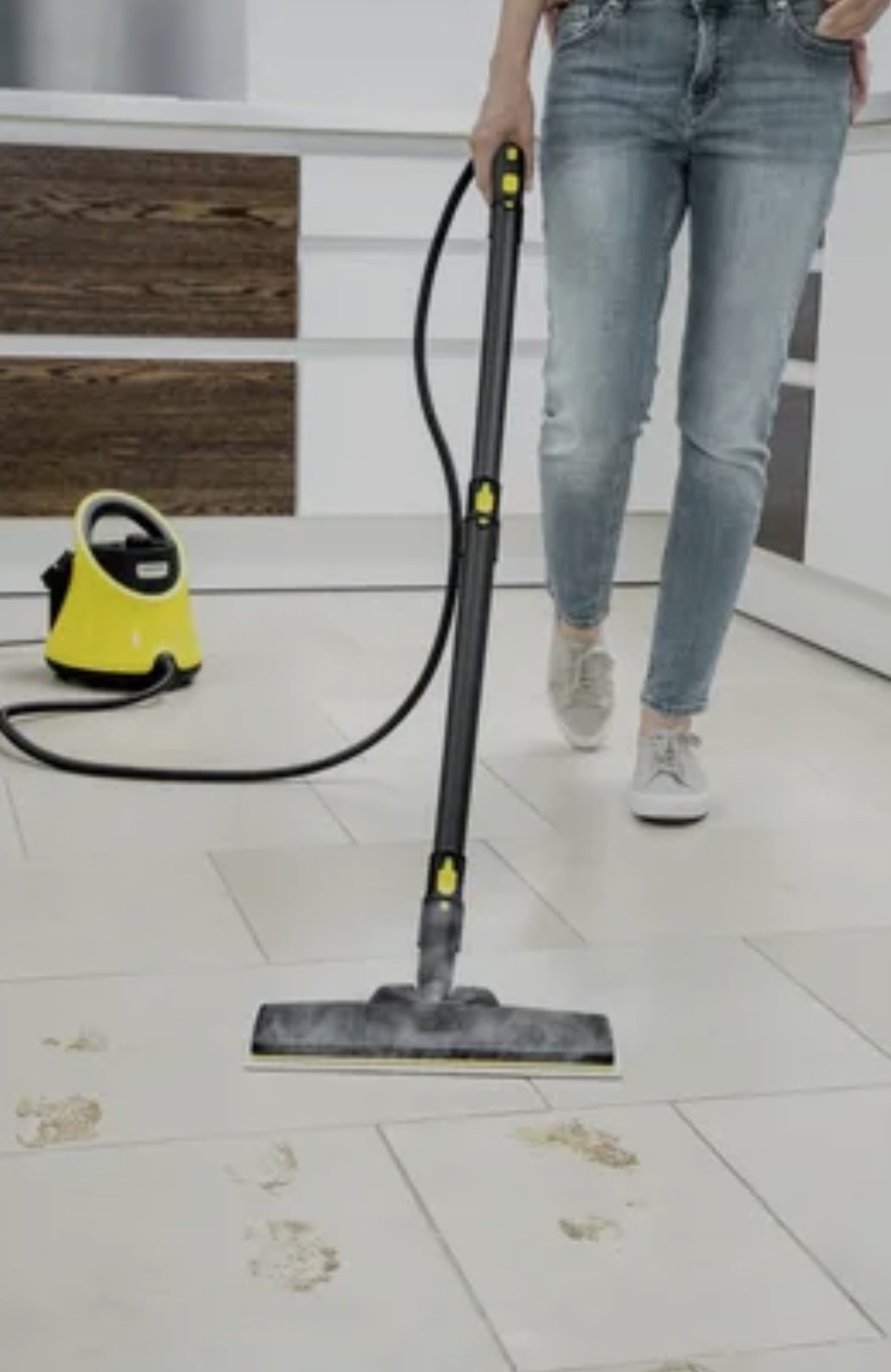Czyszczenie podłogi parownicą Kärcher z widocznymi śladami brudu, żółty odkurzacz parowy w tle, osoba w jeansach obsługująca urządzenie.
