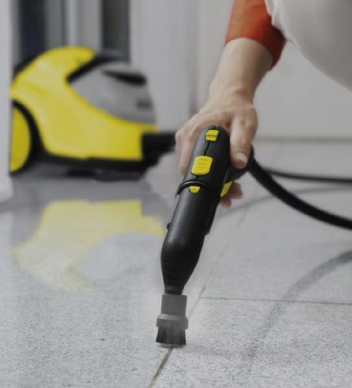 Czyszczenie fug na szarej podłodze parownicą Karcher z żółtym korpusem w tle.