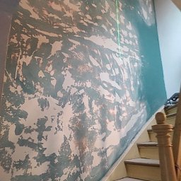 Usługi remontowo - budowlane DARBUD - Ściana w trakcie malowania z widocznymi warstwami farby i zieloną linią lasera, obok schody z drewnianą balustradą.