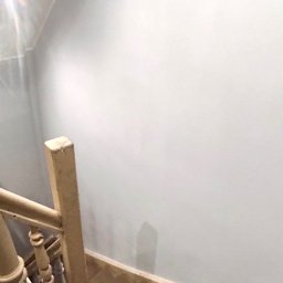 Usługi remontowo - budowlane DARBUD - Schody drewniane z jasną balustradą, świeżo pomalowana ściana w kolorze jasnoszarym, widok z góry.