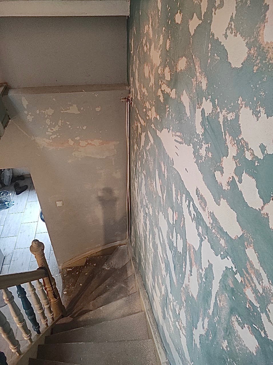 Klatka schodowa w trakcie przygotowywania ścian do malowania, widoczne ślady po zdrapywaniu starej farby, surowe schody i fragment balustrady.