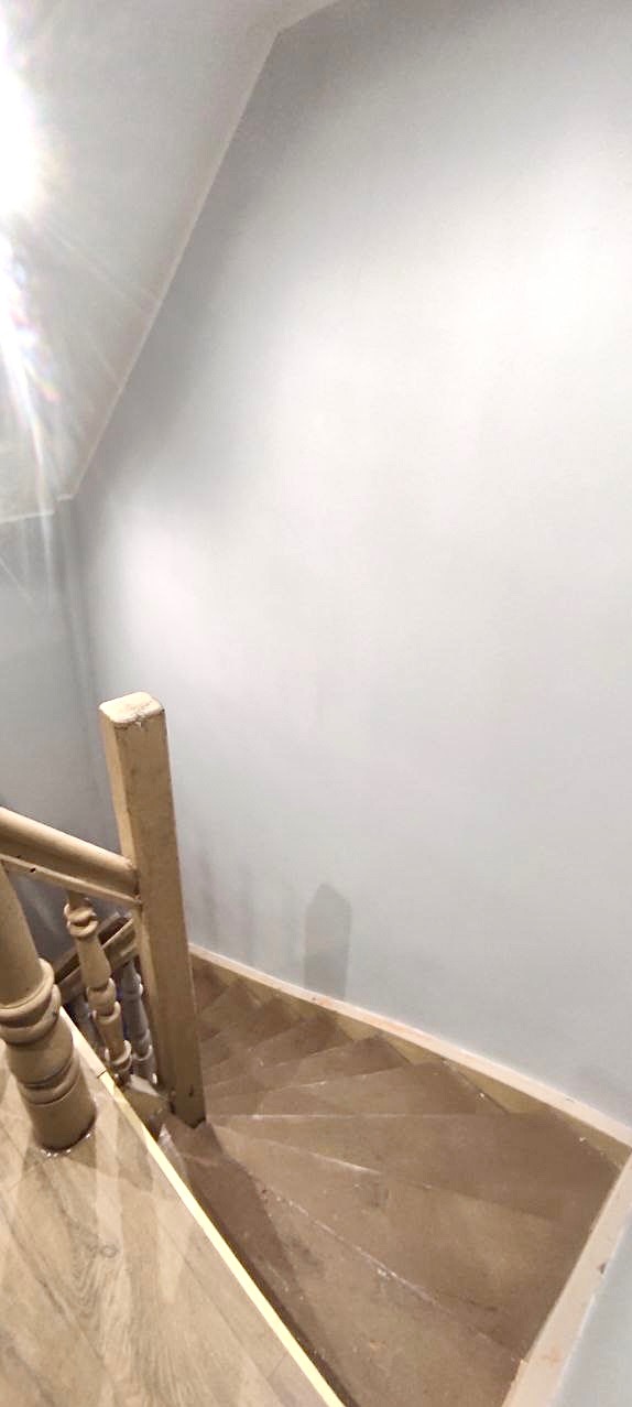 Schody drewniane z jasną balustradą, świeżo pomalowana ściana w kolorze jasnoszarym, widok z góry.