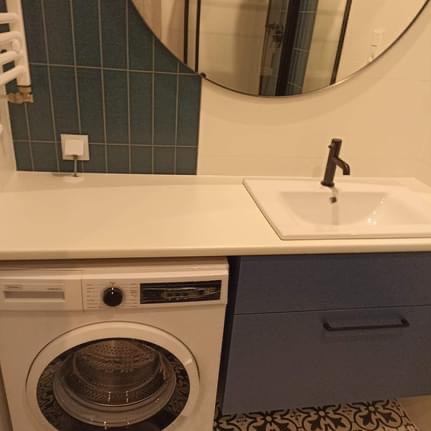 Nowoczesna łazienka z białą pralką, umywalką nablatową z czarną armaturą i okrągłym lustrem na ścianie z zielonymi płytkami.