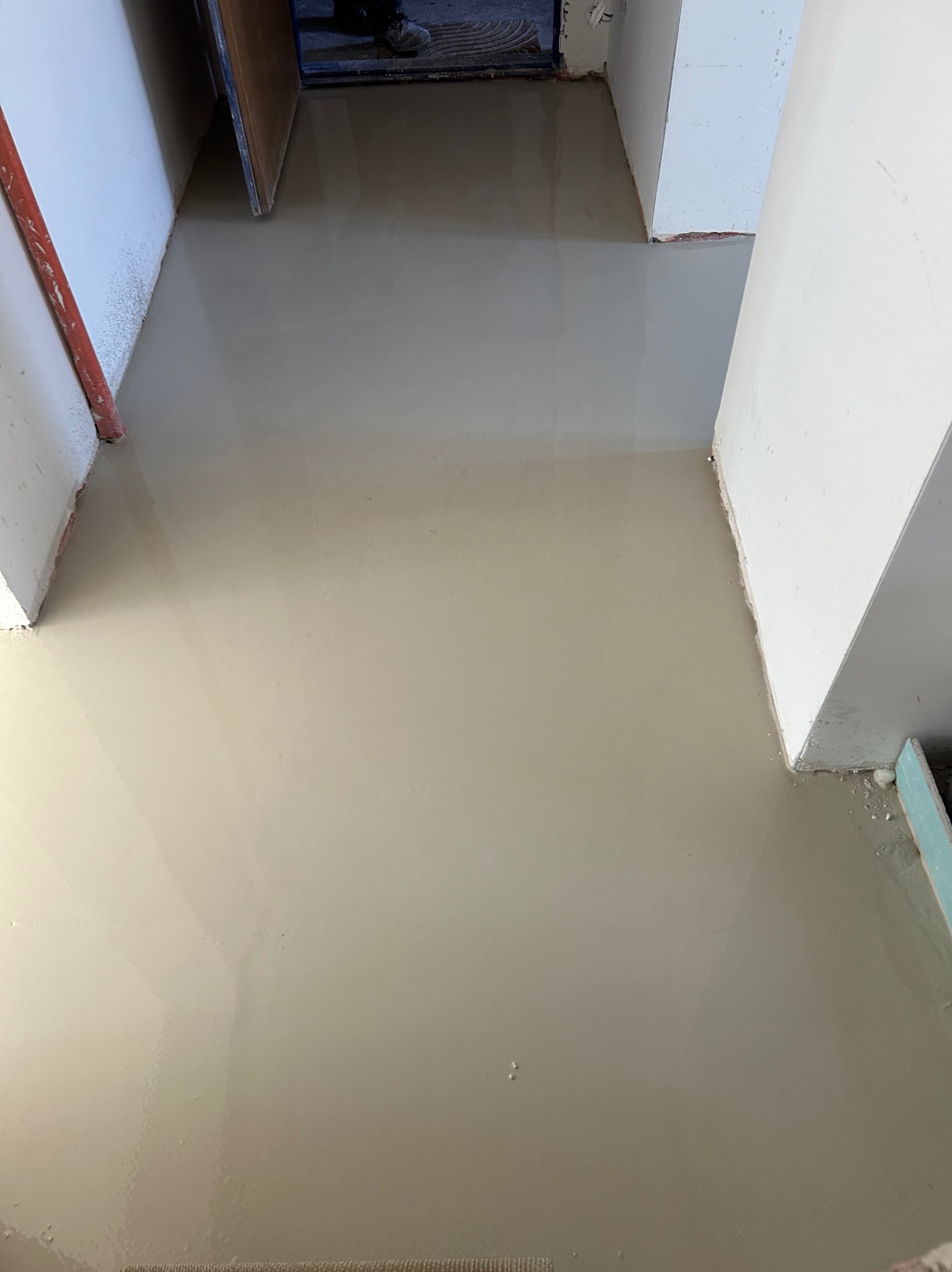 Świeżo wylana, samopoziomująca wylewka podłogowa w korytarzu, widoczne ślady wilgoci i niedoskonałości na powierzchni, przygotowana do dalszych prac wykończeniowych.