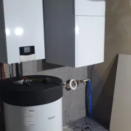 Bojler i dwa piece marki Vaillant zamontowane na szarej ścianie, na podłodze kartony zabezpieczające przed zabrudzeniem