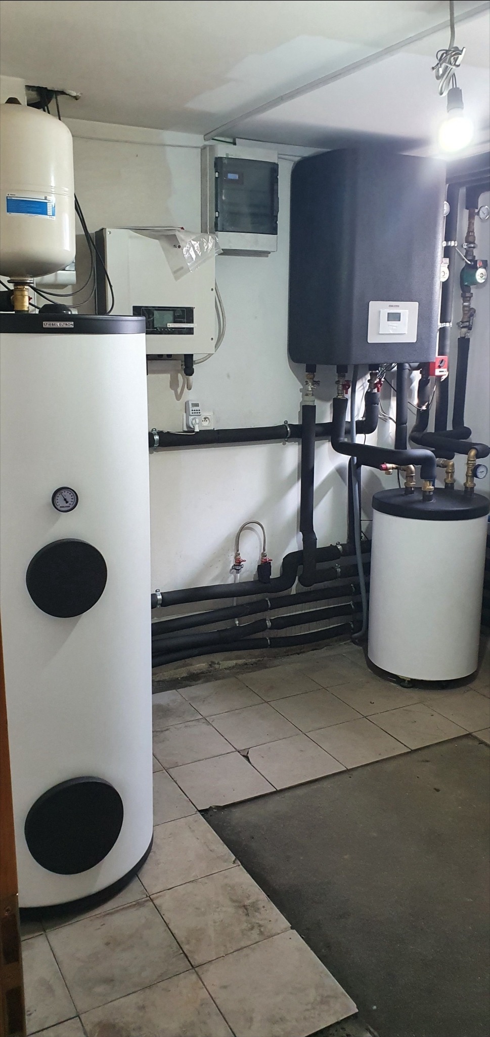 Instalacja z dwoma zbiornikami buforowymi Stibel Eltron i rozdzielnicą elektryczną w Pucku, rury izolowane termicznie, płytki podłogowe w beżach.