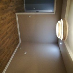 Tesmedia - Wnętrze pokoju po odświeżeniu: ściany pomalowane na beżowo, drewniane panele podłogowe, nowoczesna lampa sufitowa, okno dachowe.