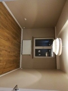 Wykończone wnętrze pokoju w Aleksandrowie Łódzkim: ściany pomalowane na beżowo, jedna ściana wyłożona panelami imitującymi drewno, biały grzejnik pod oknem, nowoczesna lampa na ścianie.