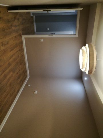 Wnętrze pokoju po odświeżeniu: ściany pomalowane na beżowo, drewniane panele podłogowe, nowoczesna lampa sufitowa, okno dachowe.