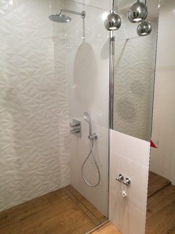 Nowoczesna kabina prysznicowa z deszczownicą, drewnopodobną podłogą i trójwymiarową białą ścianą, oświetlona wiszącymi chromowanymi lampami.
