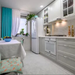 Jasna kuchnia z białymi meblami, turkusowymi akcentami w postaci zasłon i poduszek z flamingami, kwiatami w oknie i dekoracyjnymi butelkami na blacie.