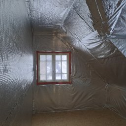 Usługi Ogólnobudowlane SIM-BUD Łukasz Simjak - Poddasze z oknem i izolacją termiczną pokrytą folią aluminiową, widoczne skosy i podłoga z płyt OSB.