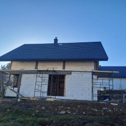 Usługi Ogólnobudowlane SIM-BUD Łukasz Simjak - Wznoszenie ścian domu z białego bloczka w Soblówce, widoczne rusztowania i nowa, ciemna dachówka na częściowo ukończonym budynku.