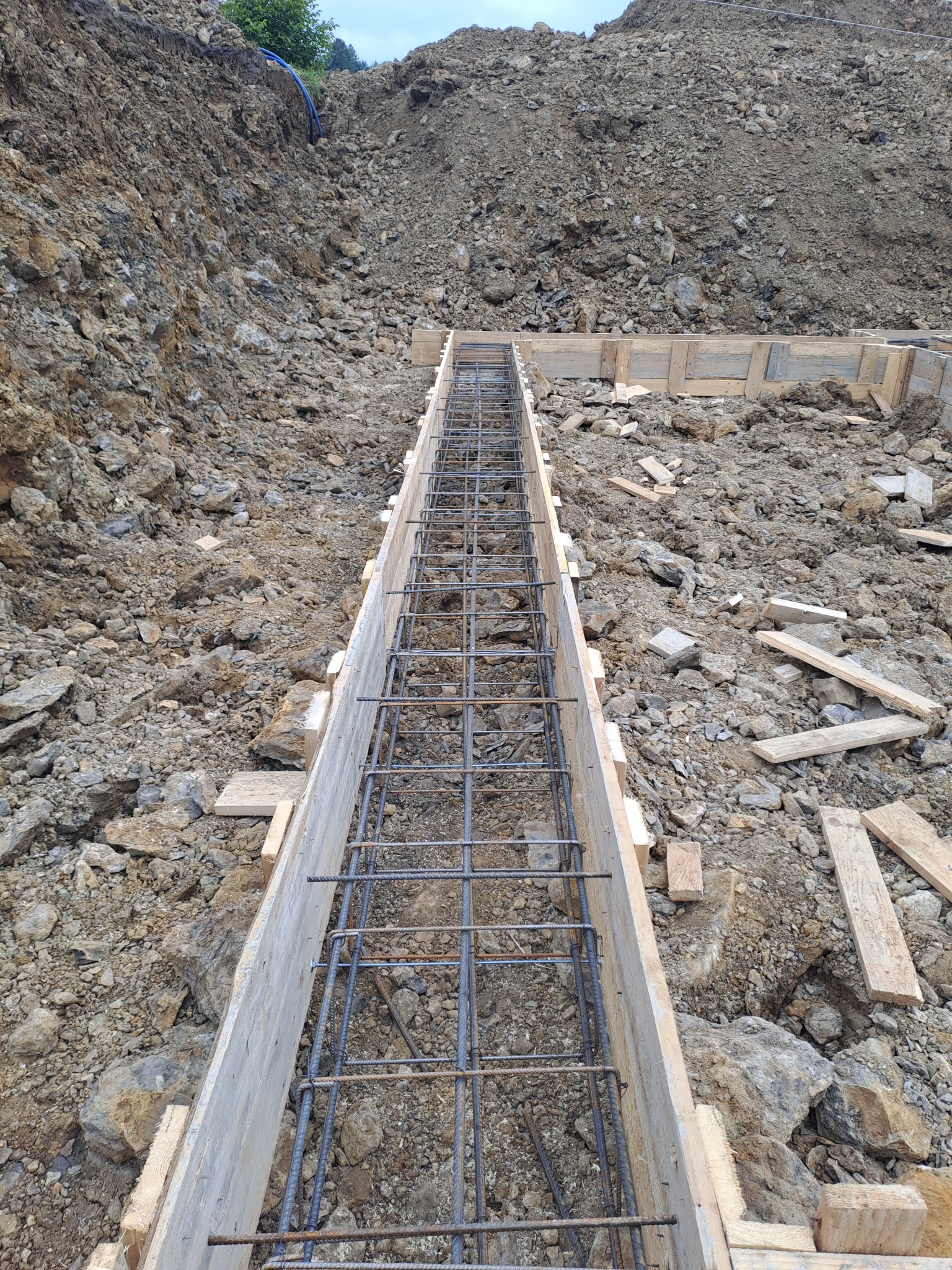 Wykonanie szalunku i zbrojenia pod fundament liniowy w wykopie ziemnym, widoczne drewniane deski i stalowe pręty zbrojeniowe.