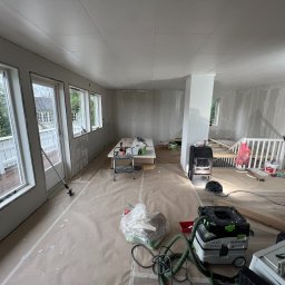 iForm - Dobrze Zbudowany s.p. Z.o.o. - Pokój w trakcie remontu: ściany pokryte gładzią, podłoga zabezpieczona folią malarską, widoczny odkurzacz przemysłowy Festool, drabina, stolik roboczy i narzędzia malarskie.