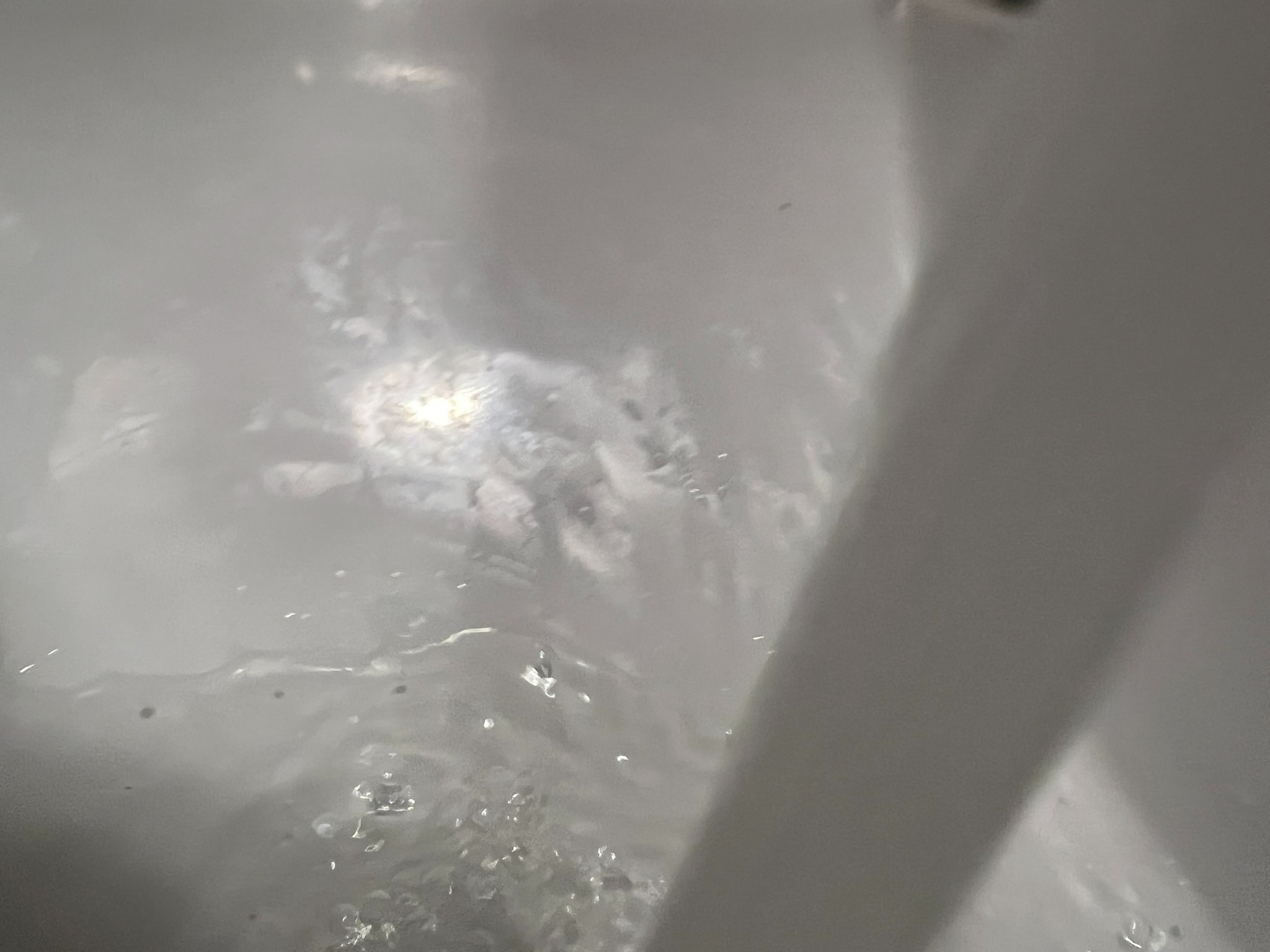 Woda spływająca po białej, ceramicznej powierzchni umywalki, widoczne krople i refleksy świetlne.