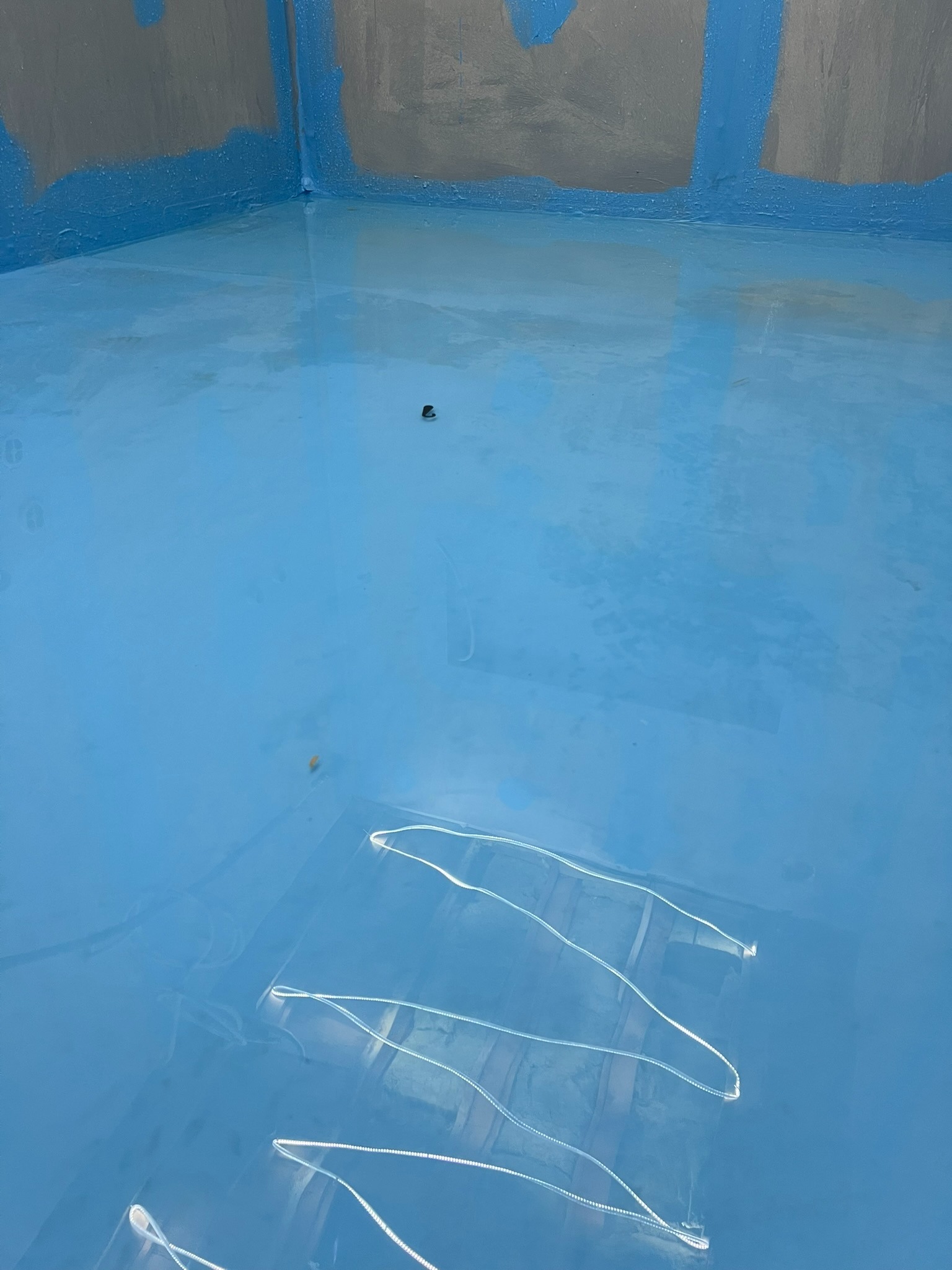 Świeżo wylana, jasnoniebieska żywica epoksydowa na podłodze łazienki, z widocznymi śladami po taśmie malarskiej na ścianach zabezpieczonych folią.