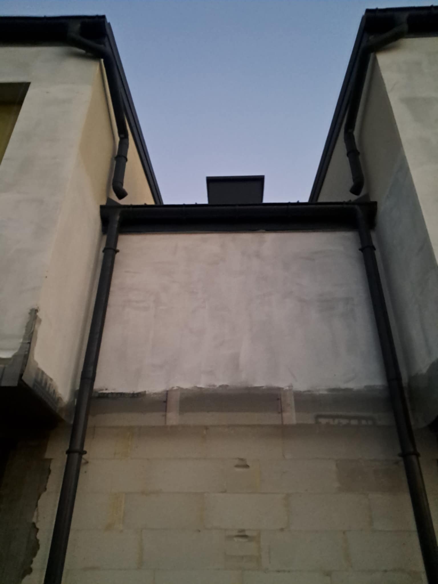 Surowy stan budynku w Warszawie z widocznymi elementami konstrukcyjnymi, w tym orynnowaniem i fragmentami ścian przed wykończeniem.