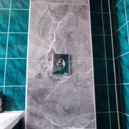 Nowoczesna toaleta z szarą płytką imitującą marmur i turkusowymi akcentami. Widoczny fragment wanny. Czyste, wykończone wnętrze łazienki.