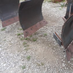 F.H.U Gabriel Kowalski - Części metalowe do maszyny rolniczej, prawdopodobnie lemiesze pługa, z widocznymi śladami spawania i mocowania na tle żwirowego podłoża.