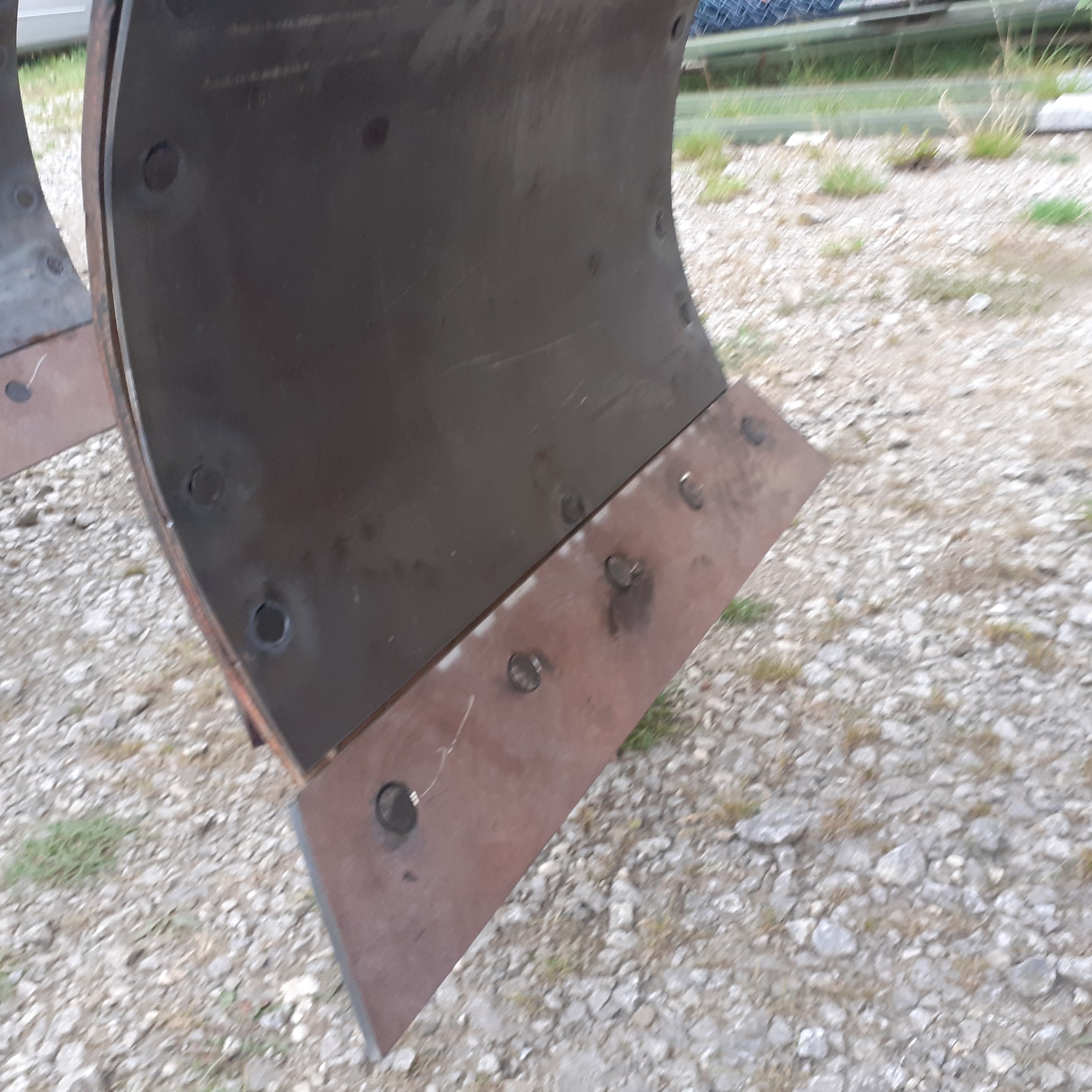 Fragment metalowej konstrukcji spawanej z widocznymi nitami i śladami spawania, leżącej na żwirowym podłożu.