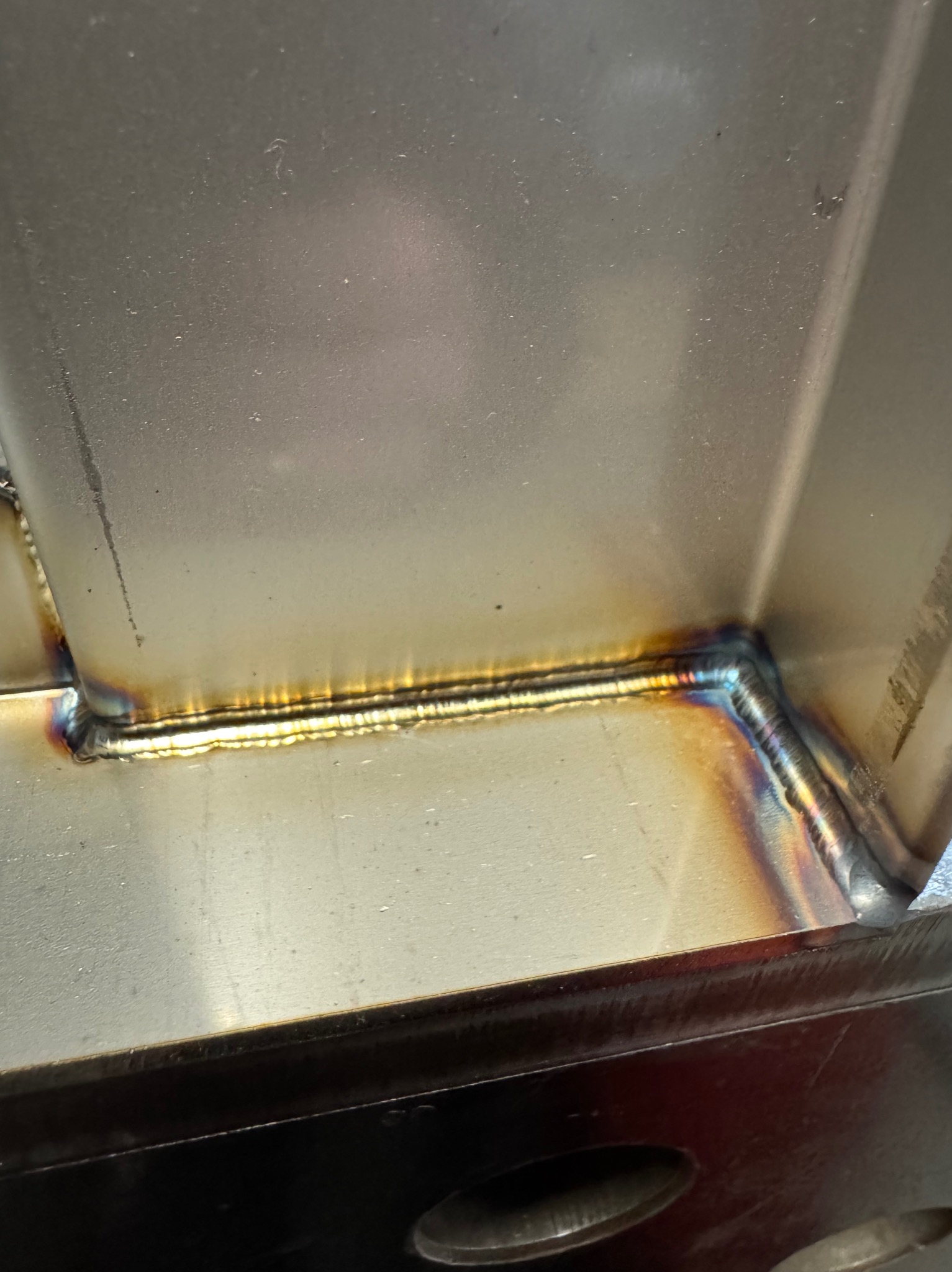 Precyzyjne spawy narożnikowe na metalowej konstrukcji, widoczne charakterystyczne, opalizujące przebarwienia termiczne wzdłuż spoin.