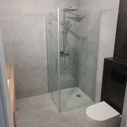 Andrii Rybchak - Nowoczesna łazienka z kabiną prysznicową typu walk-in, szare płytki na ścianach i podłodze, wisząca toaleta i ciemny panel dekoracyjny z ukrytym systemem spłukiwania.