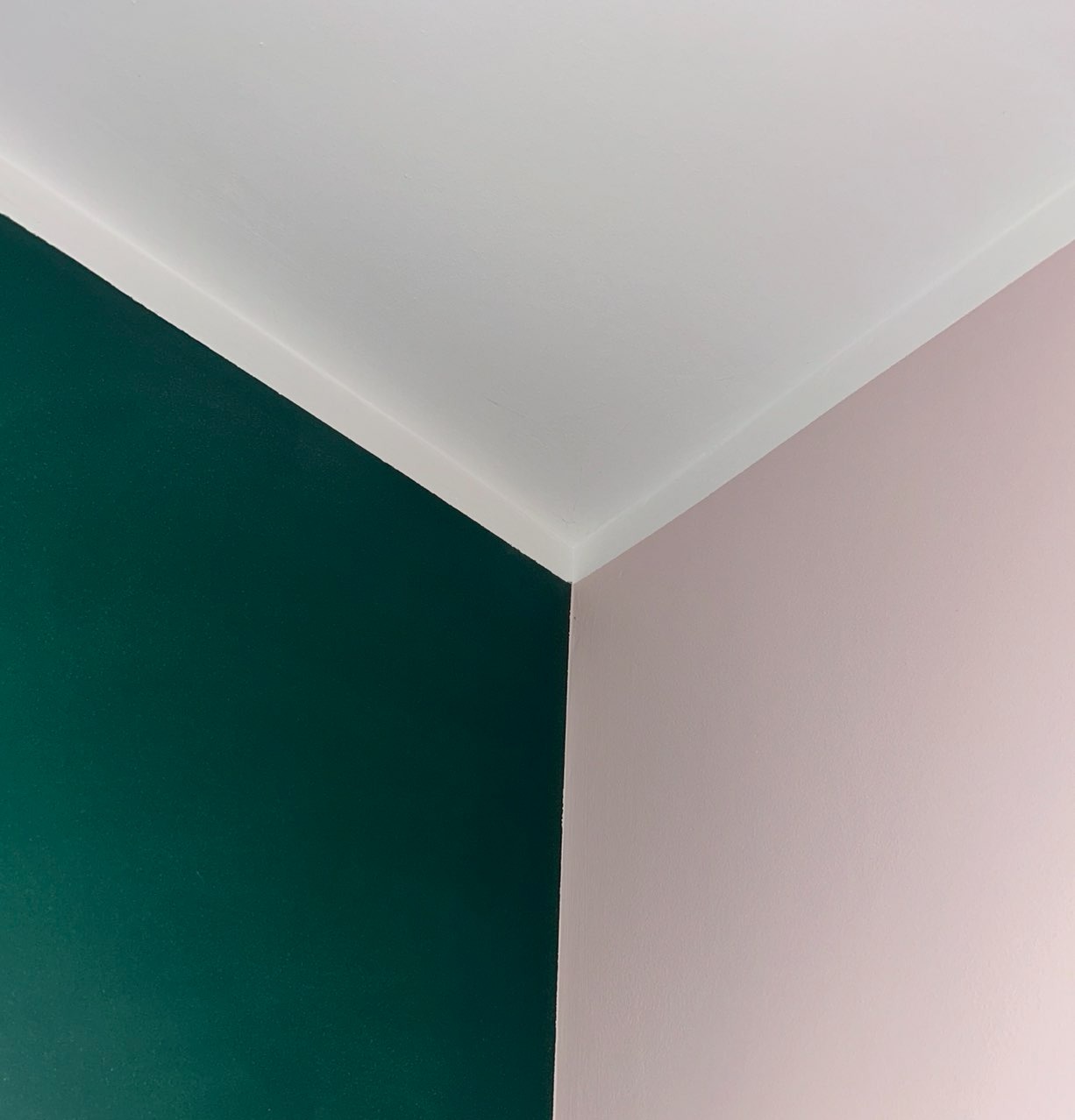 Fragment wnętrza po remoncie: ściany pomalowane na ciemnozielony i pudrowy róż, oddzielone białym narożnikiem, widok z dołu.