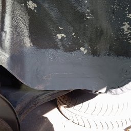 Bilard Garage - Wnętrze nadkola samochodu po zabezpieczeniu antykorozyjnym, z widocznymi śladami starej powłoki i nową, szarą warstwą ochronną. Widoczne opony i elementy zawieszenia.