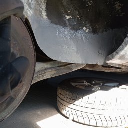 Bilard Garage - Wnętrze nadkola po zabezpieczeniu antykorozyjnym, widoczny element zawieszenia i opona. Szara, świeżo nałożona powłoka ochronna. Elementy metalowe z widoczną korozją.