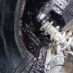 Bilard Garage - Wnętrze nadkola po zabezpieczeniu antykorozyjnym, widoczny element zawieszenia. Czarna, błyszcząca powłoka ochronna.