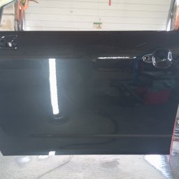 Bilard Garage - Polakierowane na czarno drzwi samochodowe z widoczną klamką, uchwytem i odblaskiem światła, w warsztacie z ceglanymi ścianami i narzędziami.