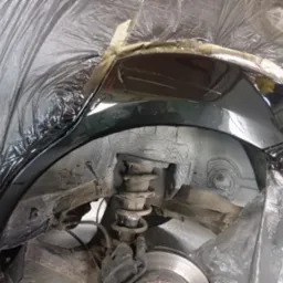 Zabezpieczone nadkole auta po nałożeniu warstwy ochronnej, widoczna sprężyna zawieszenia i elementy układu hamulcowego. Prace blacharsko-lakiernicze w toku.