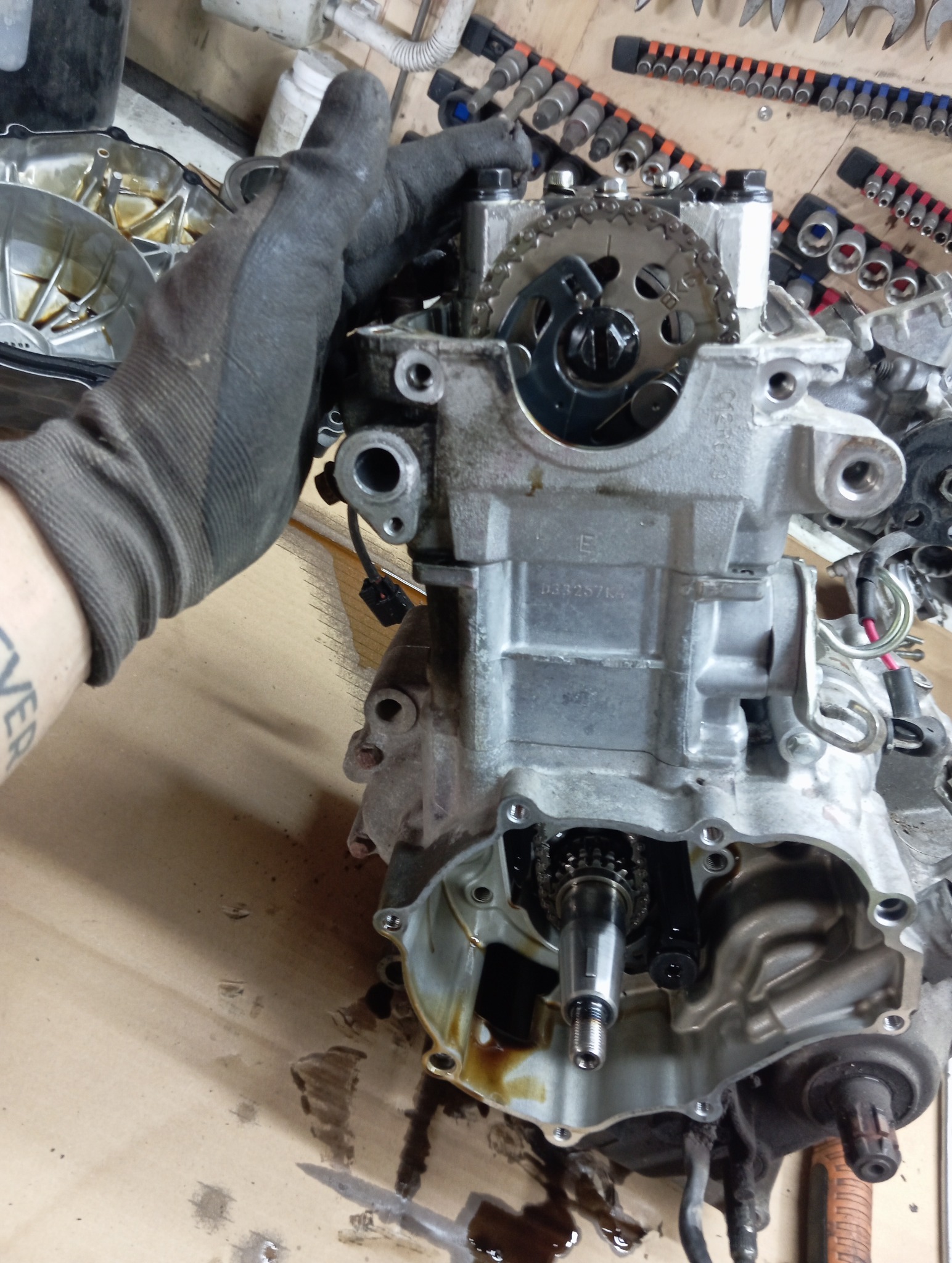 Silnik motocyklowy w trakcie naprawy: widoczna ręka w rękawicy, łańcuch rozrządu i narzędzia. Detaliczny widok na mechanizm z bliska.