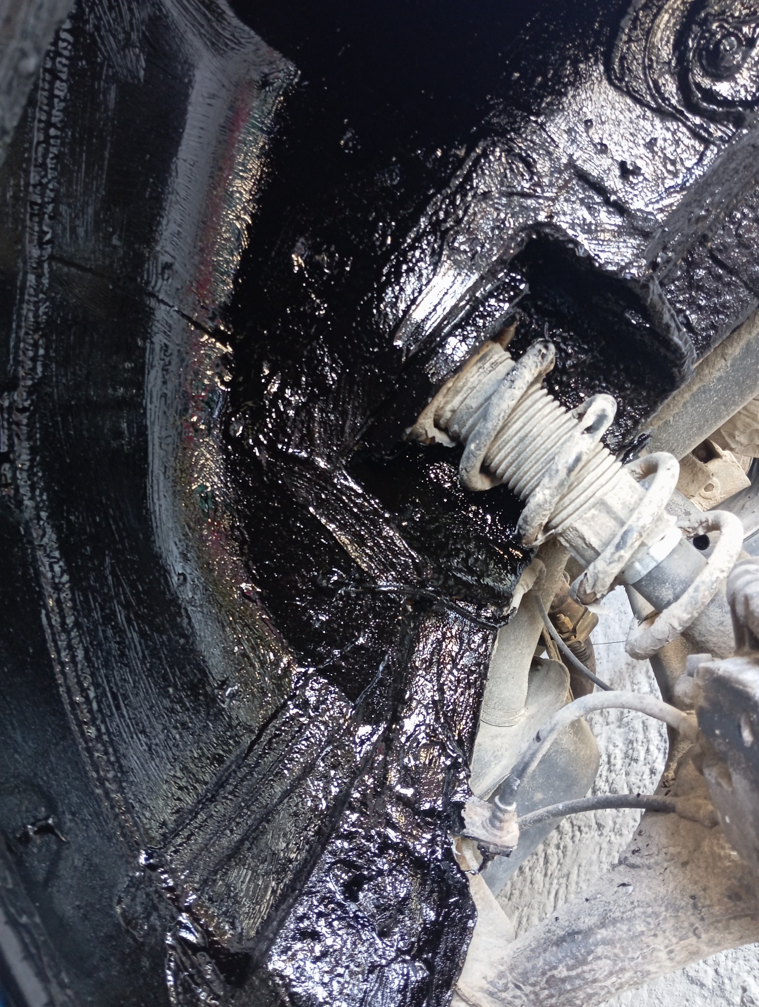 Wnętrze nadkola po zabezpieczeniu antykorozyjnym, widoczny element zawieszenia. Czarna, błyszcząca powłoka ochronna.