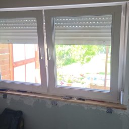 FENIX LINE SPÓŁKA Z OGRANICZONĄ ODPOWIEDZIALNOŚCIĄ - Białe okno PCV z roletami zewnętrznymi w trakcie montażu, widoczne narzędzia i fragment wnętrza z surową ścianą.