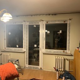 FENIX LINE SPÓŁKA Z OGRANICZONĄ ODPOWIEDZIALNOŚCIĄ - Montaż okien PCV w mieszkaniu: widoczne okna Salamander z folią ochronną, pianka montażowa, drabina i grzejnik. Wnętrze w trakcie prac wykończeniowych.