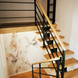 Drewniane schody z czarną metalową balustradą i drewnianą poręczą, na ścianie dekoracyjny motyw z żurawiami, widok z g&oacute;ry.
