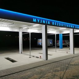 ZEKO STAL ZBIGNIEW MALIK - Konstrukcja stalowa z niebieskim oświetleniem LED nad wejściem do bezdotykowej myjni samochodowej 24h, widoczne kratki odpływowe w posadzce i elementy montażowe.