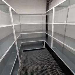 Półki metalowe w surowym, industrialnym stylu z kratownicą podłogową, widoczne rury pod sufitem.