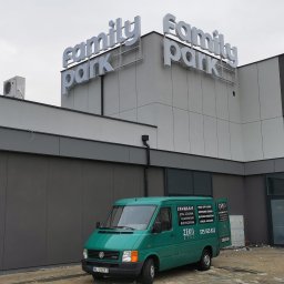 ZEKO STAL ZBIGNIEW MALIK - Zielony bus firmy Zeko Stal z reklamą spawania stali czarnej, aluminium i nierdzewnej na tle budynku z napisem Family Park.