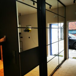 ZEKO STAL ZBIGNIEW MALIK - Nowoczesne drzwi przesuwne z czarnymi szprosami i lustrzanymi panelami, widoczne oświetlenie sufitowe i fragment wnętrza w trakcie remontu.