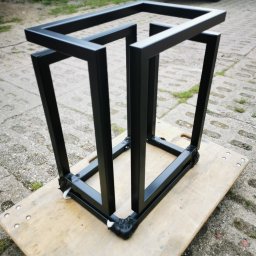 ZEKO STAL ZBIGNIEW MALIK - Czarna, metalowa konstrukcja spawana z profili kwadratowych, zabezpieczona taśmą na rogach, umieszczona na płycie OSB na zewnątrz, z widocznym fragmentem samochodu dostawczego w tle.