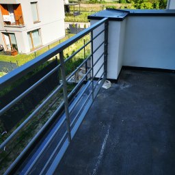 ZEKO STAL ZBIGNIEW MALIK - Nowoczesna balustrada balkonowa z poziomych, stalowych profili w Legionowie, widok z góry na czarną, gumową nawierzchnię balkonu i fragment budynku mieszkalnego w tle.