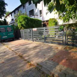 Nowoczesna, pozioma brama wjazdowa z szarych, metalowych profili, z tabliczką 'Solid Security', przed budynkiem mieszkalnym i zaparkowanym zielonym vanem firmy z branży metalowej.