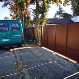 ZEKO STAL ZBIGNIEW MALIK - Nowa, brązowa brama wjazdowa z metalowymi panelami, widziana z ulicy w słoneczny dzień, z zielonym samochodem dostawczym firmy obok, na tle jesiennych drzew i domu.