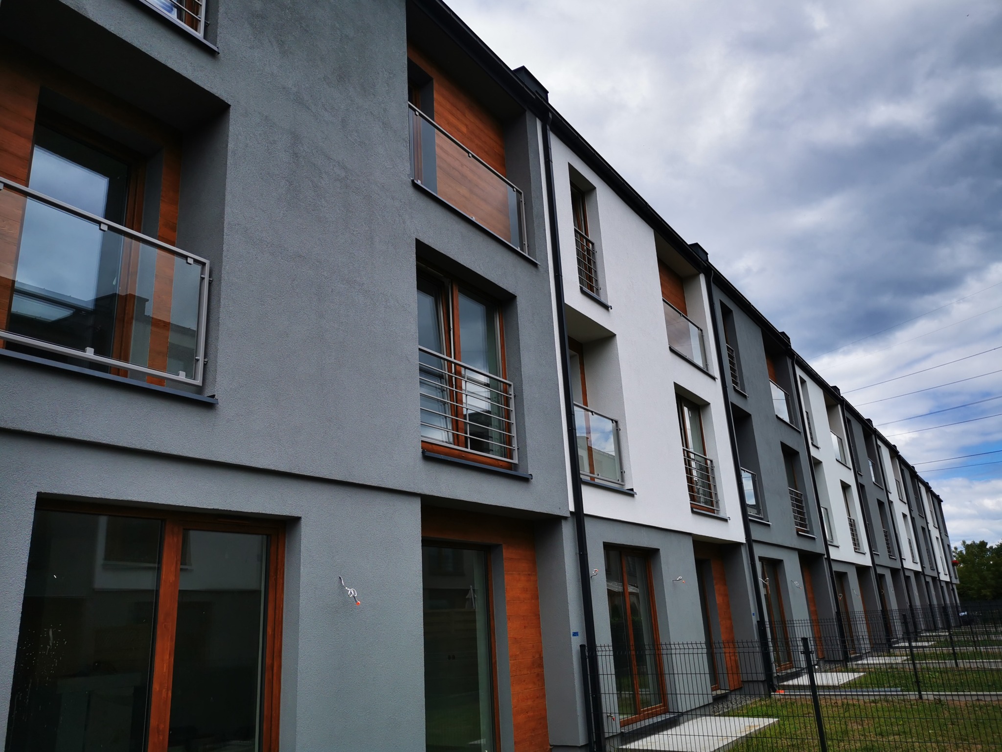 Szereg identycznych, nowoczesnych budynków mieszkalnych z balkonami z balustradami szklanymi i stalowymi, pomalowanych w odcieniach szarości i bieli, widzianych pod kątem z poziomu gruntu,...